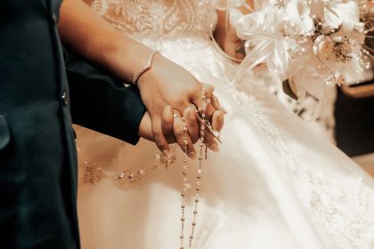 Close-up of a bride and groom holding hands with a rosary at their wedding in Tlaxcala, Mexico.