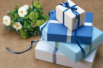 Three beautifully wrapped gift boxes with blue ribbons arranged beside a floral bouquet.