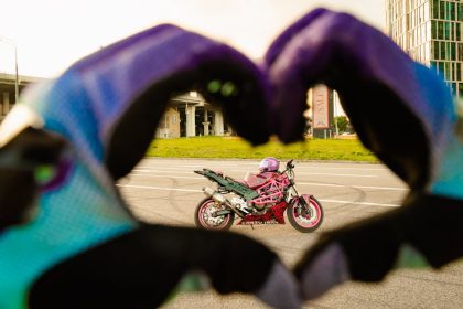 Vibrant pink motorcycle framed by heart-shaped hand gesture with gloves.
