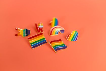 A vibrant collection of LGBT pride pins featuring rainbow flags and symbols on an orange backdrop.