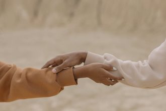 Close-up view of two hands reaching and holding each other against a muted background, symbolizing connection.