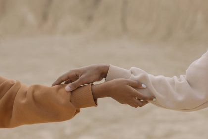Close-up view of two hands reaching and holding each other against a muted background, symbolizing connection.