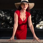 A woman in a red dress and hat leaning on a ledge