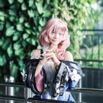 A pink-haired cosplayer posing against a vibrant green backdrop indoors.