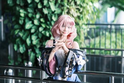 A pink-haired cosplayer posing against a vibrant green backdrop indoors.