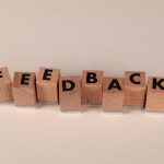 Blocs de lettres en bois disposés pour écrire « FEEDBACK » sur fond neutre. Idéal pour les concepts de communication.