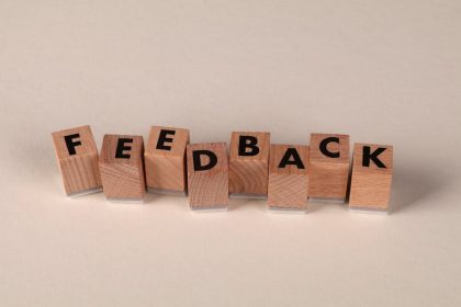 Blocs de lettres en bois disposés pour écrire « FEEDBACK » sur fond neutre. Idéal pour les concepts de communication.