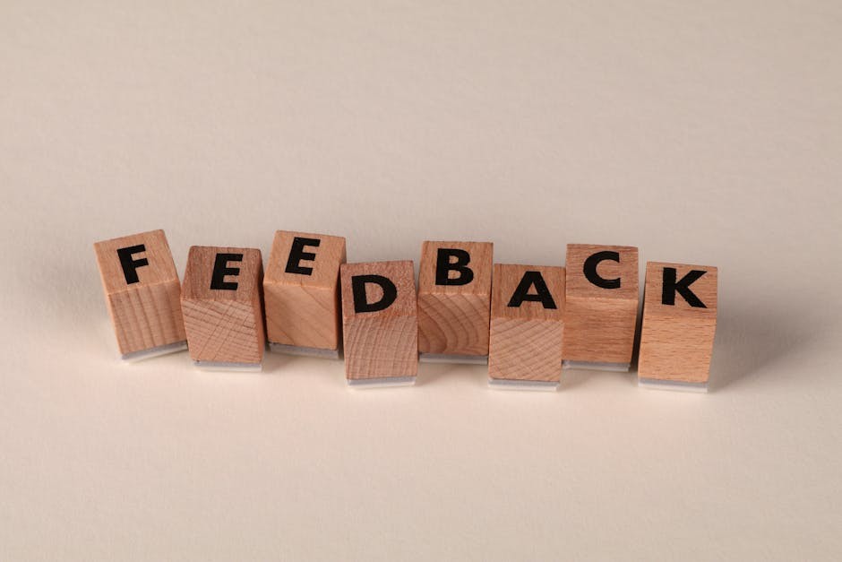 Blocs de lettres en bois disposés pour écrire « FEEDBACK » sur fond neutre. Idéal pour les concepts de communication.