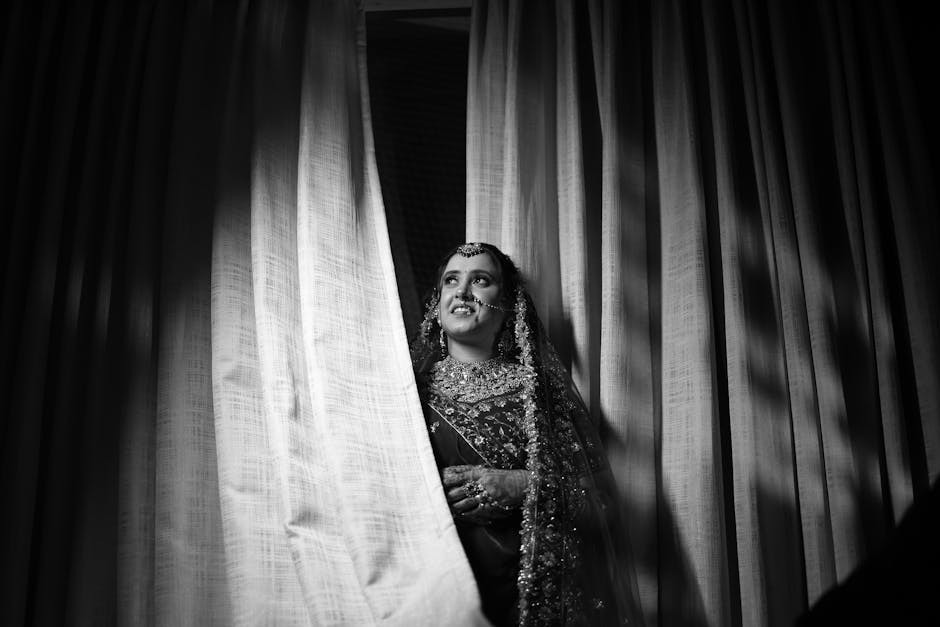 Magnifique portrait en noir et blanc d'une mariée indienne en tenue traditionnelle, près d'un rideau.
