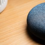 Gros plan d'une enceinte connectée posée sur une table en bois, révélant les détails de sa texture.