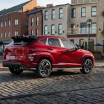 Un élégant SUV Hyundai Kona rouge stationné à l'extérieur sur une rue pavée, près de bâtiments historiques.