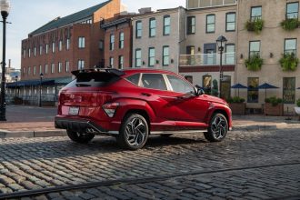 Un élégant SUV Hyundai Kona rouge stationné à l'extérieur sur une rue pavée, près de bâtiments historiques.