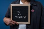 Personne tenant un tableau de lettres avec le message 'Pas mon Président' et une épinglette du drapeau américain.
