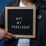 Personne tenant un tableau de lettres avec le message 'Pas mon Président' et une épinglette du drapeau américain.