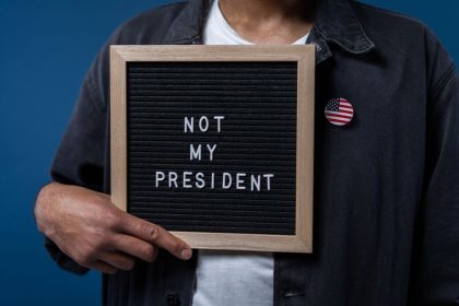 Personne tenant un tableau de lettres avec le message 'Pas mon Président' et une épinglette du drapeau américain.