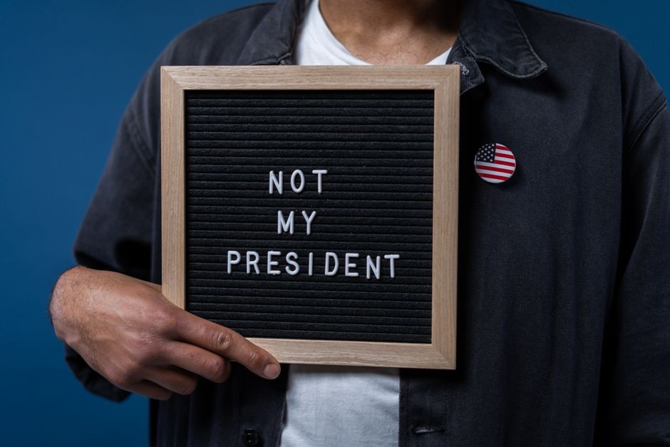 Personne tenant un tableau de lettres avec le message 'Pas mon Président' et une épinglette du drapeau américain.