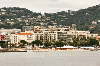 Vue panoramique d'un complexe hôtelier de luxe sur le front de mer de Cannes, mettant en valeur une architecture élégante sur fond de collines luxuriantes.